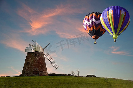 日落时分，在天空充满活力的山顶上，热气球在旧风车上飞舞，这是一幅可爱的画面