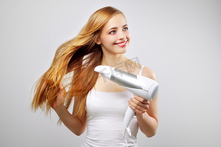 发型美女摄影照片_美丽的微笑女孩干燥用吹风机吹干头发