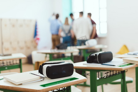 虚拟现实耳机在桌上与老师和高中学生站立在教室后面