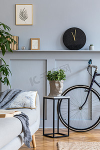 用灰色沙发、相框、植物、枕头、大理石凳子、自行车和时尚家居装饰的典雅个人配饰装饰的斯堪的纳维亚客厅室内设计. 
