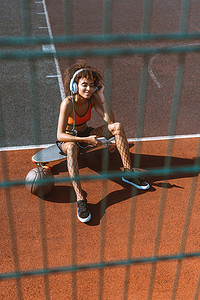 年轻的非裔美国女性，在运动服在耳机听音乐，坐在退潮在运动场
