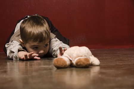 小孩伸手摄影照片_小孩伸手去拿泰迪熊的地板上爬行