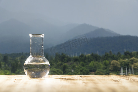 在山背景上木制的桌子上的玻璃实验室瓶的清洁水。生态概念，纯度和质量的水试验.