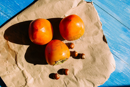 柿子成熟的谎言在牛皮纸上蓝色的木制背景，附近的淡褐色的褐色坚果的谎言组上。素食营养。健康饮食、 dietin