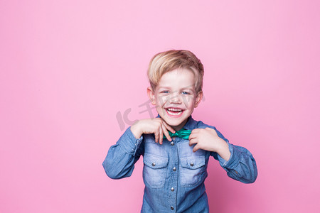 儿童理发摄影照片_Young handsome kid smiling with blue shirt and butterfly tie. Studio portrait over pink background