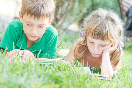 绿色阅读摄影照片_两个年轻快乐的孩子，孩子们阅读的书籍上自然酒泉
