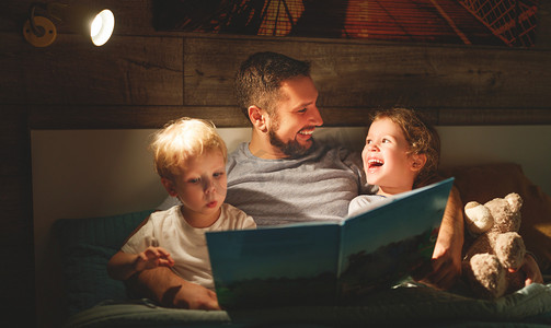 故事童话故事摄影照片_晚上家庭读书。父亲读孩子。前一本书