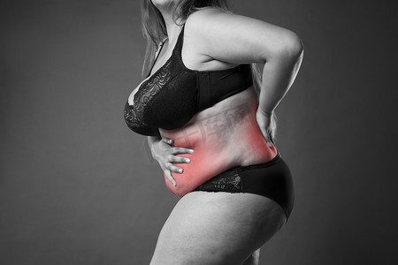 背部和腹部的疼痛，背痛，超重女性的身体，在灰色的背景上的胖女人