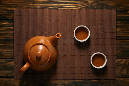 春节狗摄影照片_在竹垫上可以看到棕色陶瓷茶壶和茶杯的顶视图