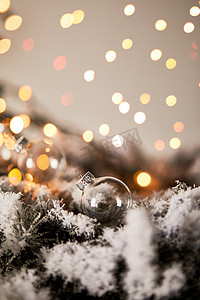 圣诞树摄影照片_雪中的云杉树枝上的透明的圣诞球，黄灯模糊