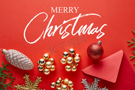 明亮的圣诞装饰、信封和红色背景的thuja的顶部视图，附有圣诞快乐的插图