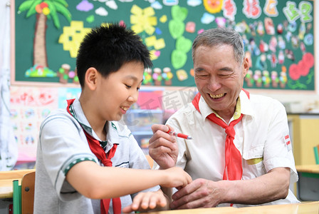 2018年5月28日，在中国东部江苏省南京市一所小学，一位身穿白衬衫、戴红领巾的老人在儿童节前与一名年轻学生合影。
