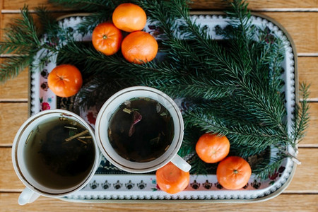 圣诞前夜，两杯花草茶放在一张桌子上，放着橘子和云杉枝。
