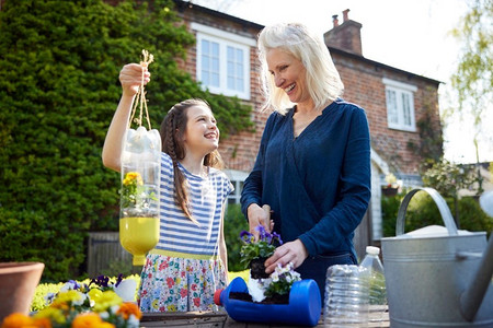 自制净水器摄影照片_母亲和女儿从塑料瓶包装废物做密封植物持有人在花园在家里
