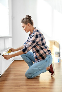 维修，改善和翻新概念—妇女与尺子测量加热器在家里。妇女与尺子测量加热器在家里