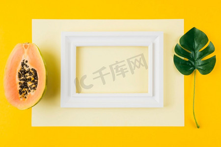 奥林巴斯数码相机.半木瓜monstera叶白色木框架纸反对黄色背景