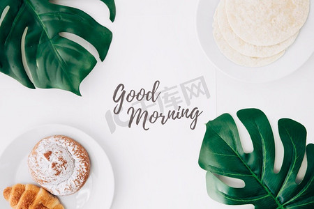 新鲜面粉玉米饼烤面包牛角面包早餐早上好文本纸绿色怪兽叶子白色背景