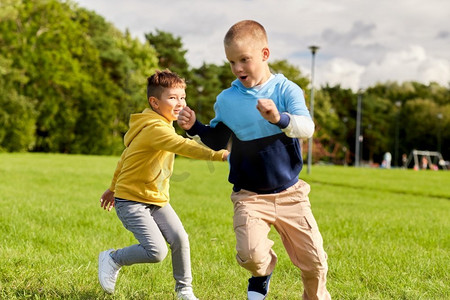 童年，休闲和人的概念—两个快乐的男孩玩标签游戏和运行在草坪在公园。两个快乐的男孩玩标签游戏在公园