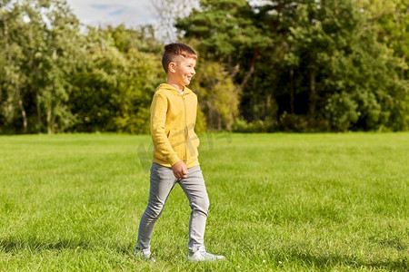 草坪和人摄影照片_童年，休闲和人的概念-快乐的男孩在公园的草坪上散步。快乐的男孩在公园的草坪上散步