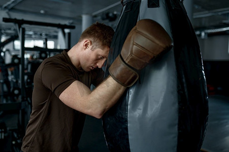 疲惫的男子拳击手拿着拳击包，在体育馆进行艰苦训练后感到非常疲惫。疲惫的拳击手拿着拳击包感到沉重的疲劳