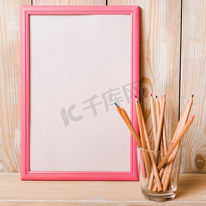 白色空白边框配粉色边框彩色铅笔玻璃架木桌
