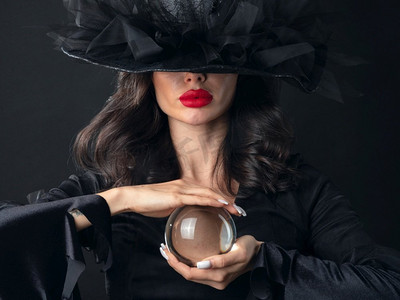 在万圣节女巫服装的美丽性感的模特妇女拿着水晶球把咒语算命。万圣节女巫女人与水晶球
