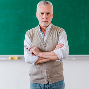 高年级男教授双手交叉站立在黑板上