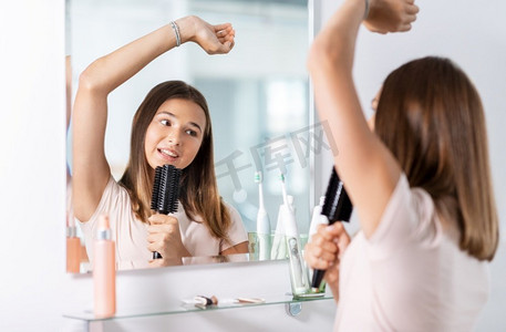 唱歌女孩摄影照片_美丽和人的概念—十几岁的女孩寻找镜子和唱歌给梳子在浴室。十几岁的女孩唱歌到发刷在浴室