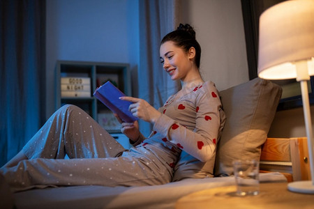 人，就寝时间和休息概念—快乐的少女在家里的床上看书在晚上。快乐的十几岁的女孩读书在床上在家里