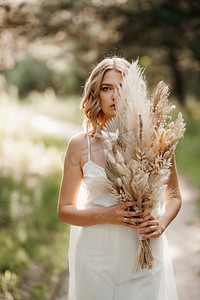一个快乐的新娘女孩在白色轻礼服与花束干花在森林路径