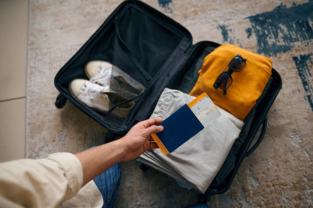 带着旅行票和护照的男子在打包的行李箱。准备好度假了。带着旅行票和护照的男子在打包的行李箱。