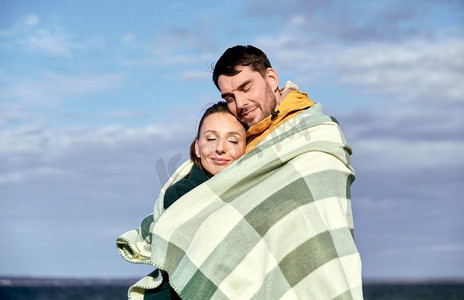 爱情，关系和人的概念-秋天海滩上，幸福的微笑着的情侣在温暖的毯子里。秋天海滩上裹着温暖毯子的幸福夫妇