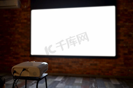 娱乐电影摄影照片_空白的电视投影机和墙上的屏幕显示电影。视频、电影或体育游戏流媒体。向观众放映电影的空白电视放映机