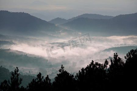 黎明时分从上方俯瞰薄雾山谷的美丽景色。山的剪影自然背景