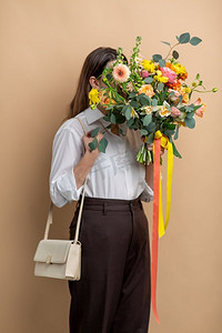 人物鲜花摄影照片_人物和花卉设计概念-米色背景上有一束鲜花的女人肖像。带着一束鲜花的女人肖像