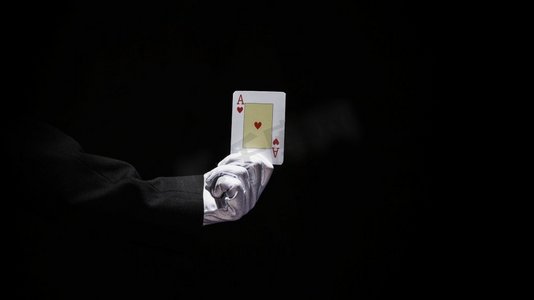 魔术师的手拿王牌扑克牌反对黑色背景