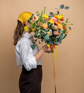 人物和花卉设计概念-米色背景上有一束鲜花的女人肖像。带着一束鲜花的女人肖像