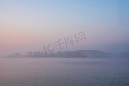 在水库湖上的春天日出的史诗风景图像与黎明的光辉散布在水与低雾添加大气