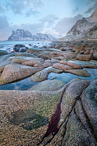日落时分，冬天的挪威海峡湾海滩上的岩石。乌塔克列夫海滩，罗福滕群岛，挪威。挪威峡湾海滩