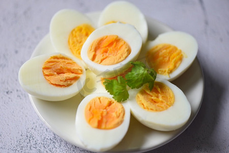 酥油蛋黄摄影照片_鸡蛋菜单食物煮鸡蛋在白色盘子装饰叶子绿色香菜，切成两半蛋黄烹饪健康吃鸡蛋早餐