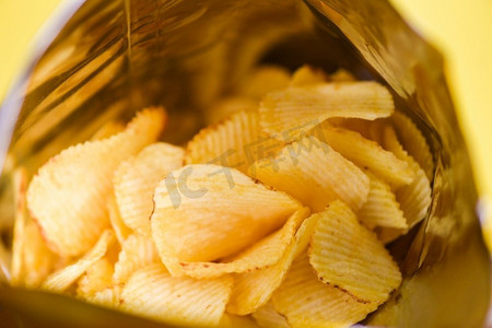 零食摄影照片_薯片是袋装的零食，包装在塑料中即食，脂肪食品或垃圾食品，薯片的黄色背景