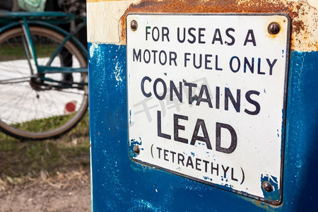 老式汽油、汽油或汽油燃料泵与铅和Tetraethyl警告标志和自行车在背景
