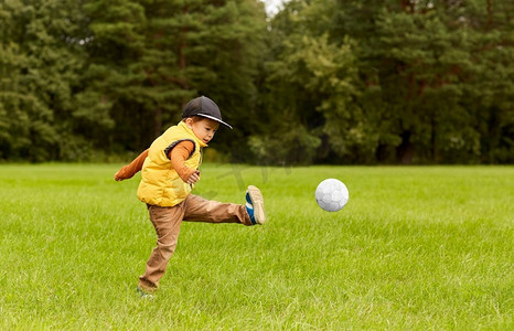 童年，休闲游戏和人的概念-快乐的小男孩在夏令营踢足球。公园里拿着球踢足球的小男孩