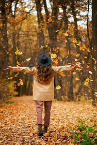 兴奋摄影照片_快乐兴奋的年轻女子下的叶子秋天。从后面看。在秋季享受宁静和放松。快乐的兴奋的年轻女子下叶子秋天
