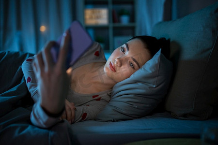 技术，就寝时间和休息概念—十几岁的女孩在睡衣与智能手机躺在床上晚上。十几岁的女孩有电话躺在床上晚上