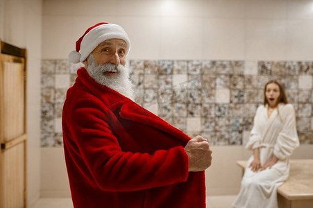 坏圣诞老人吓坏了穿着敞开的红色浴袍的女人。水疗、桑拿、蒸房的混乱局面。坏圣诞老人吓得穿着敞开浴袍的女人