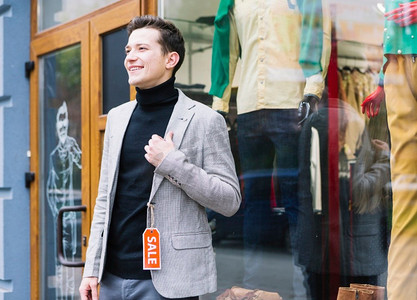 时尚的年轻人穿着夹克与销售标签站在商店外面