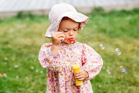 草坪和人摄影照片_童年，休闲和人的概念—快乐的小女婴吹肥皂泡在夏天。快乐的女婴吹肥皂泡在夏天