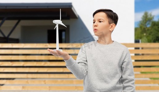 风吹儿童摄影照片_可持续能源、电力和人的概念-房屋背景上有玩具风力涡轮机的男孩。房子背景上有玩具风力涡轮机的男孩