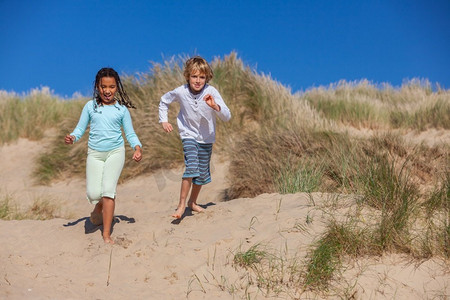 两个孩子，一个金发男孩和一个混血非洲裔美国女孩，在沙滩的沙丘上玩得很开心